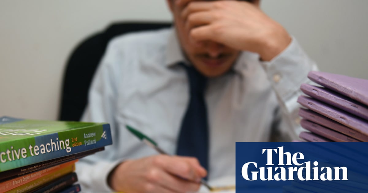 Photo of a primary school teacher looking stressed next to piles of classroom books